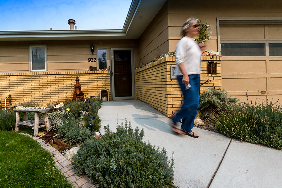 A woman with blue jeans, a grey top and sunglasses briskly walks along the accessible sidewalk leading from the home.